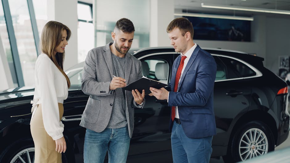 Three adults discussing documents at a car dealership beside a black car.