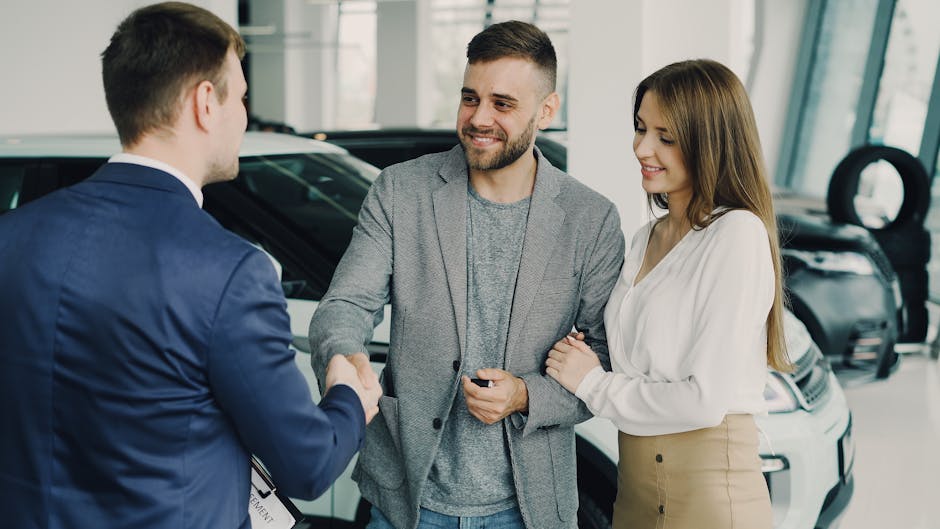 Happy couple finalizing car purchase with salesman in dealership showroom